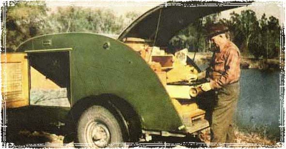 a man standing in front of a green truck next to a body of water and trees