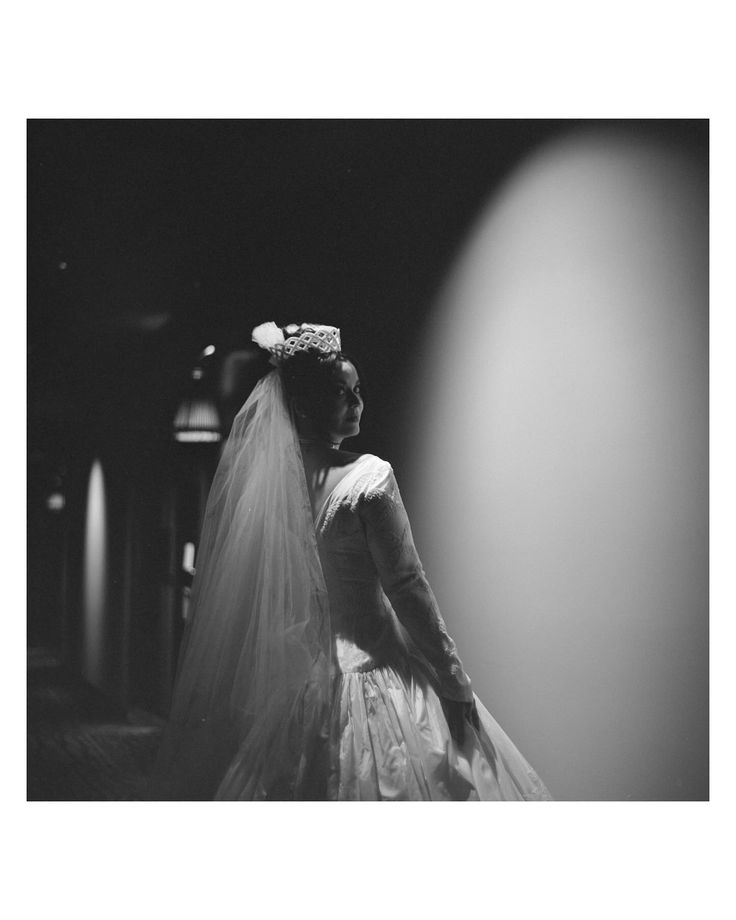 a black and white photo of a woman in a wedding dress looking at the light