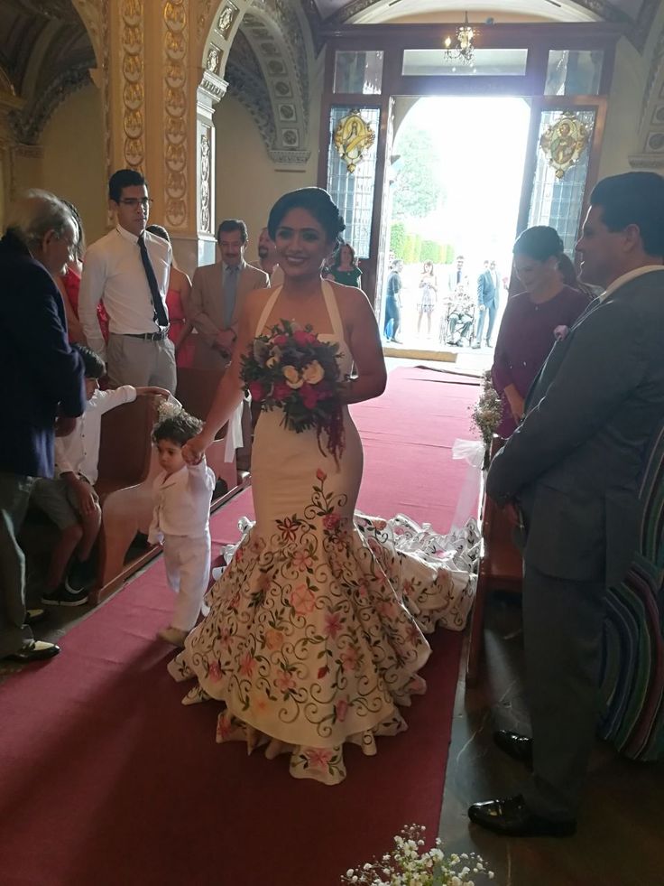 a woman in a wedding dress walking down the aisle with a small child on her lap