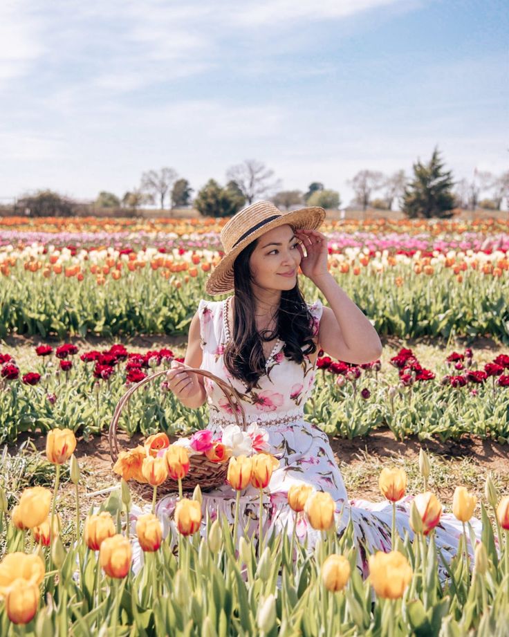 a woman sitting in a field full of tulips with a hat on her head