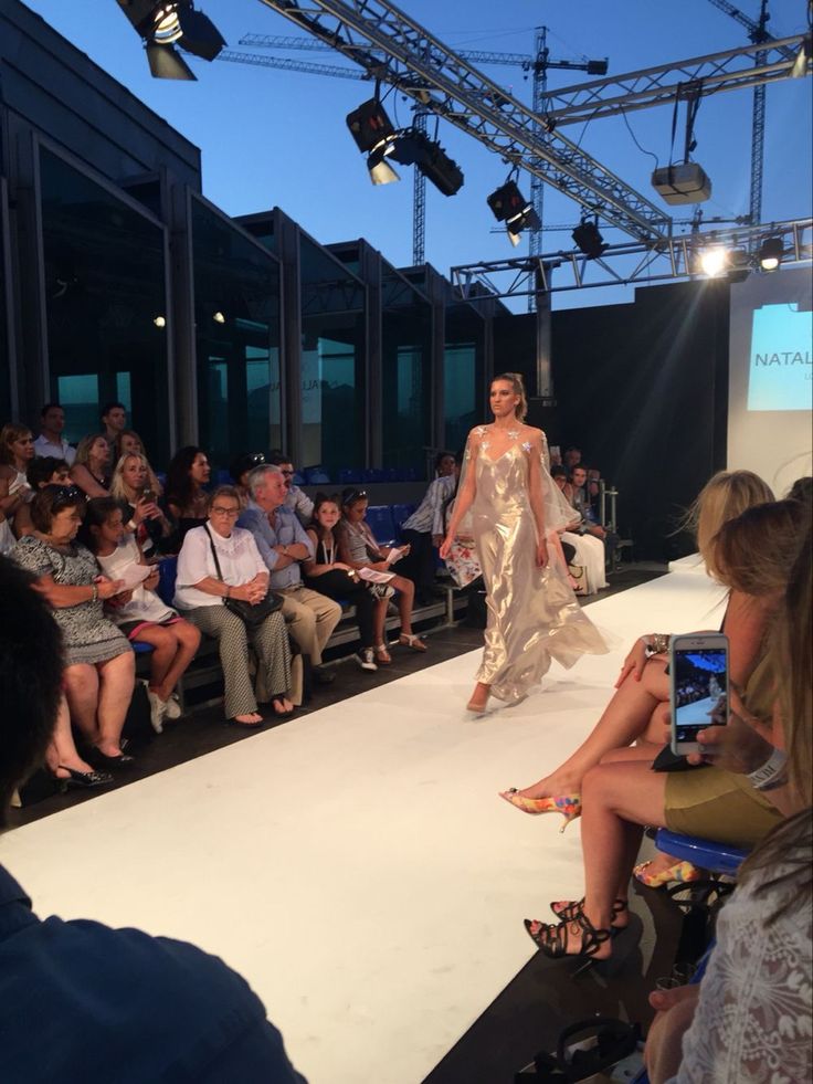 a woman is walking down the runway at a fashion show while people watch from behind her