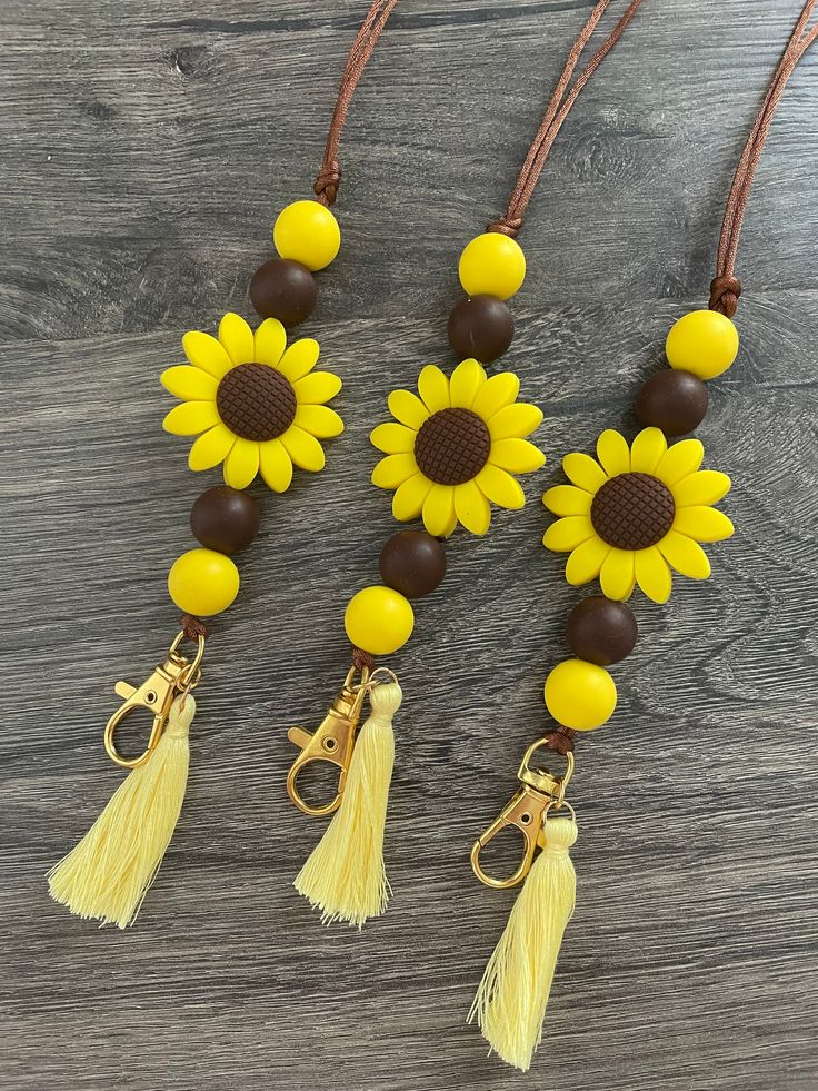 three yellow sunflowers with brown beads and tassels on a wooden table