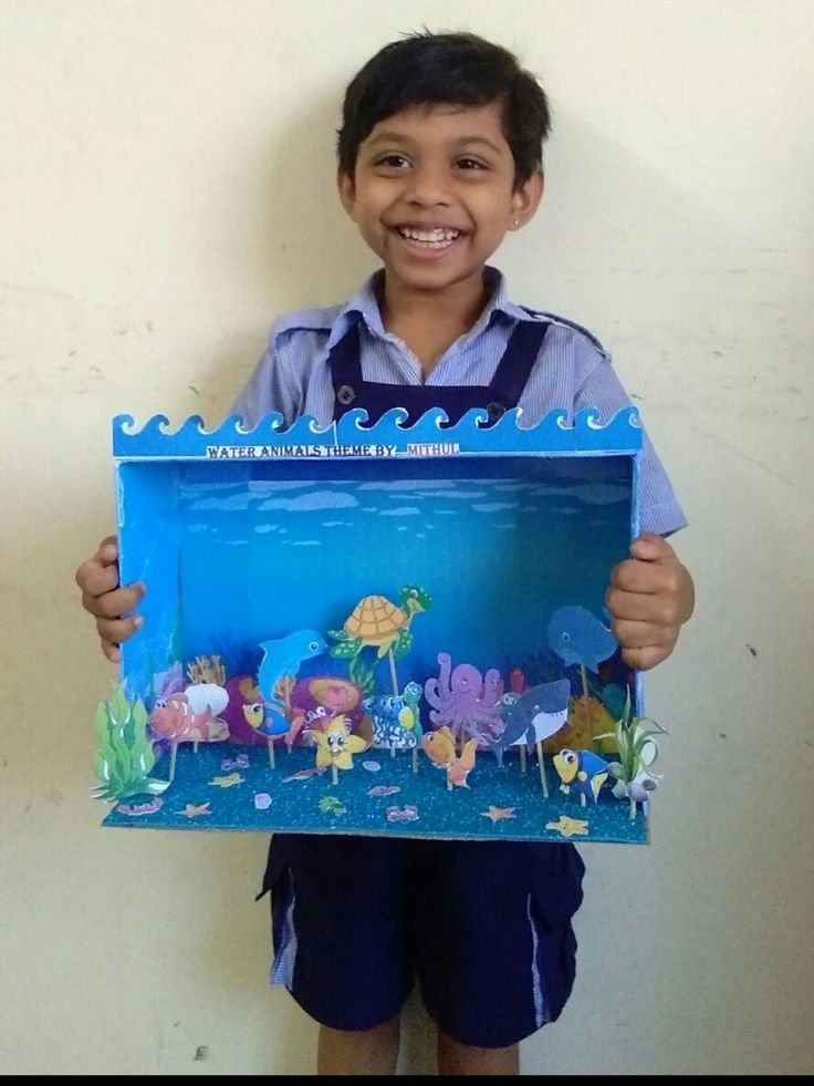 a young boy holding up a paper cut out of an ocean scene with fish and corals