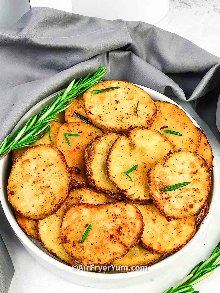 baked potato wedges in a white bowl with rosemary garnish