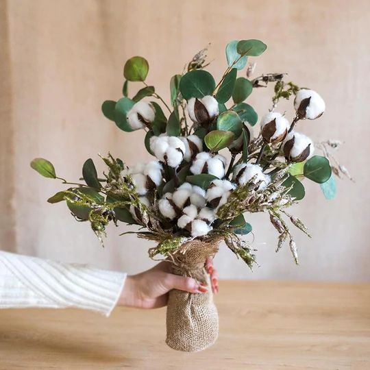 a person holding a bouquet of cotton and greenery