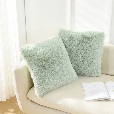 two pillows sitting on top of a couch next to an open book and a window