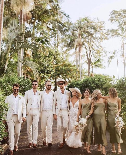 a group of people standing next to each other in front of trees and bushes at a wedding