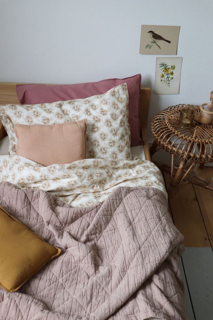 a bed with pillows and blankets on top of it next to a wicker table