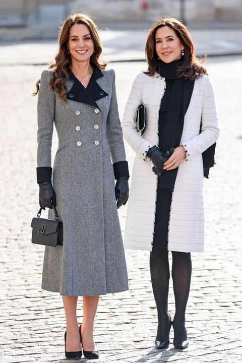 two women standing next to each other on a cobblestone street in front of a building