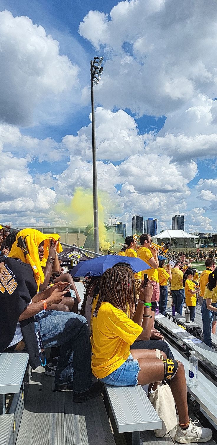 a group of people sitting on top of bleachers with umbrellas over their heads