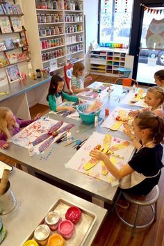 several children are sitting at a table making crafts in a store with their hands on the paper