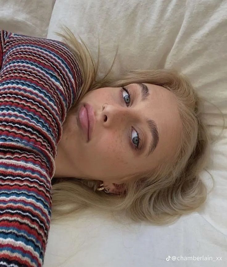 a woman laying on top of a bed next to a white pillow covered in blankets