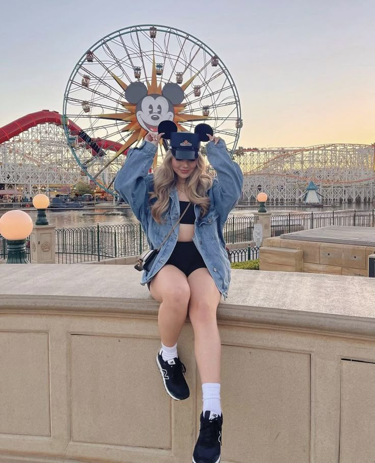 a woman sitting on top of a wall next to a ferris wheel at disneyland california adventure park