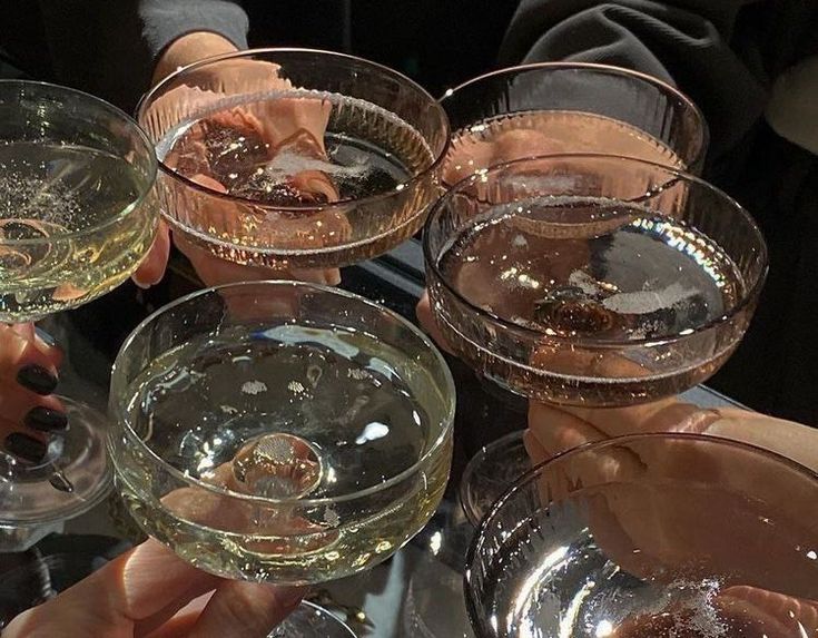 several people are holding up wine glasses on a glass table with one person's hand in the middle