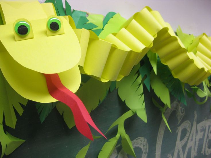 a close up of a paper snake on a wall with green leaves and red ribbon