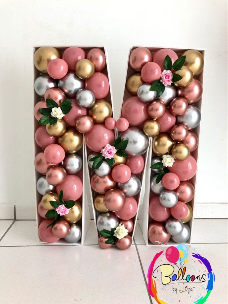 the letter m is made out of pink, silver and gold balloons with flowers on them