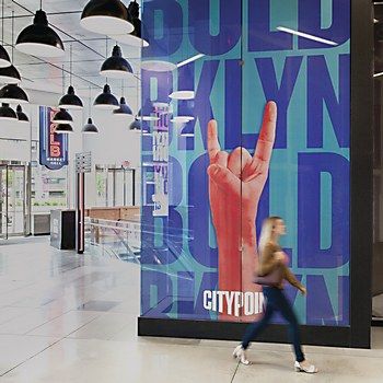 a woman walking past a large poster in a building with lights hanging from the ceiling