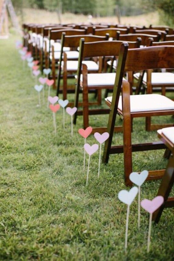 rows of wooden chairs with hearts on them in the grass at a wedding or ceremony