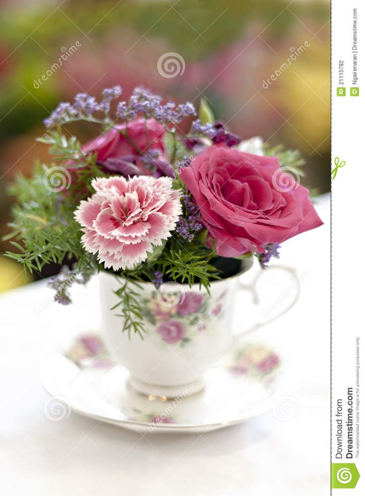 a bouquet of flowers in a teacup on a table with pink and purple flowers