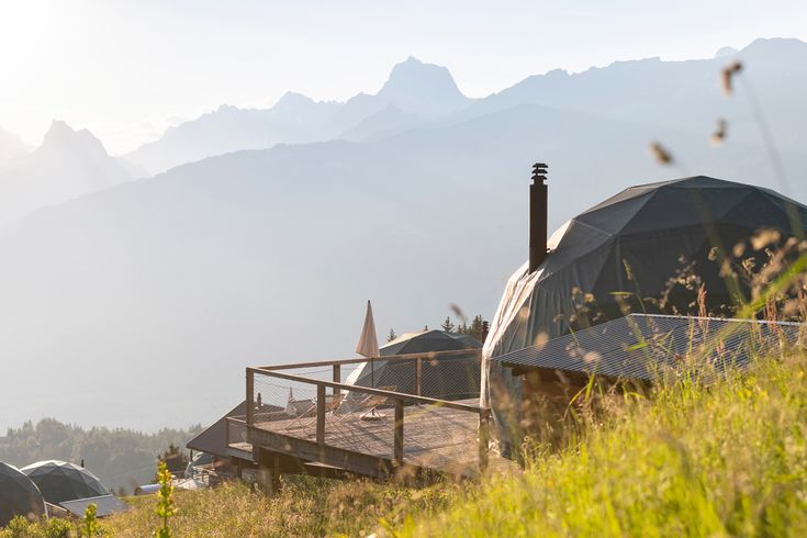 a wooden deck in front of a tent with mountains in the background and grass on the foreground