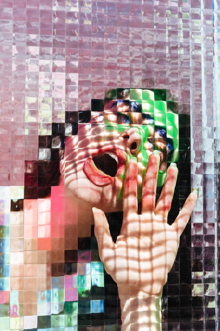 a woman's face and hands are reflected in a mosaiced glass wall with squares