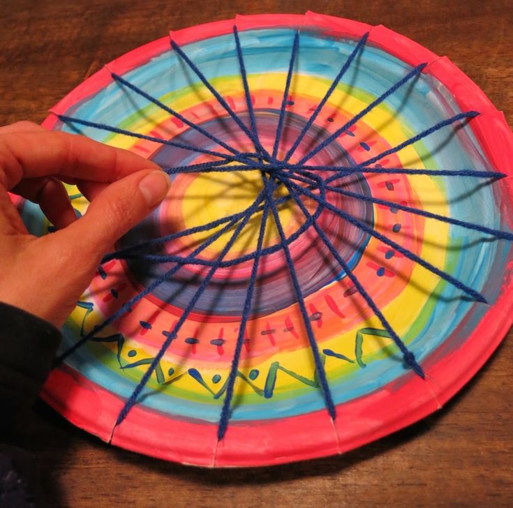 a person is holding a colorful paper plate with sticks in the center and writing on it