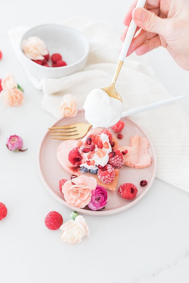 a person is spooning ice cream onto a plate with raspberries and roses