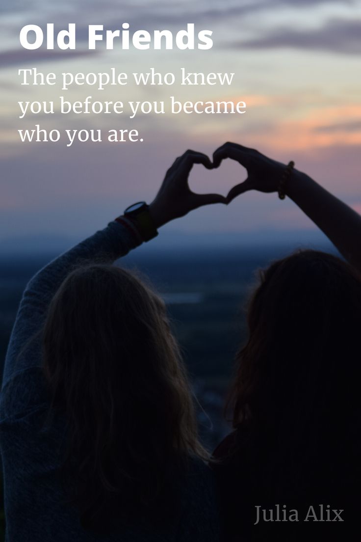 two women making a heart shape with their hands while the sun sets in the background