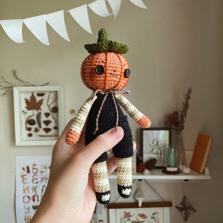 a hand holding a small crocheted pumpkin doll