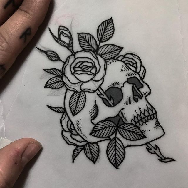 a hand holding a piece of paper with a skull and rose tattoo on it