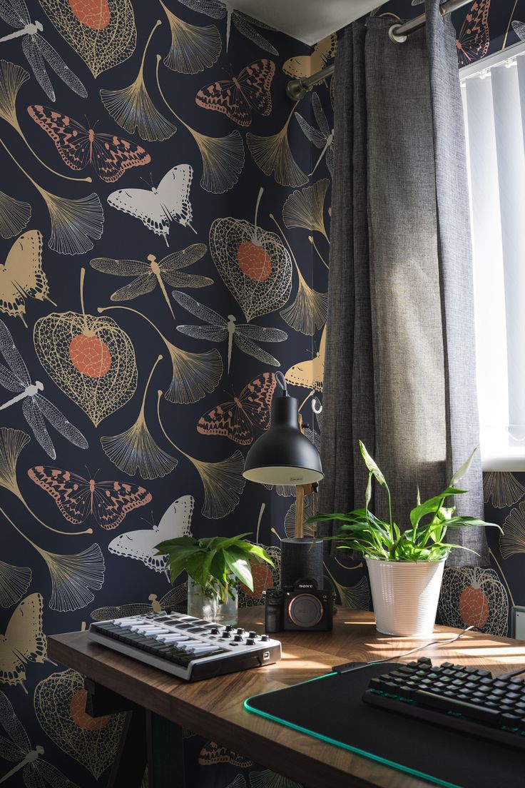 a desk with a computer, keyboard and plant in front of a wallpapered background