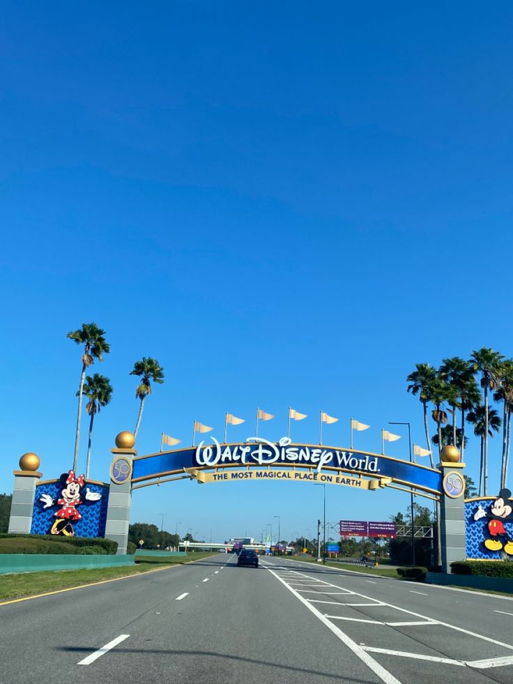 the entrance to walt world with cars driving under it and palm trees in the background