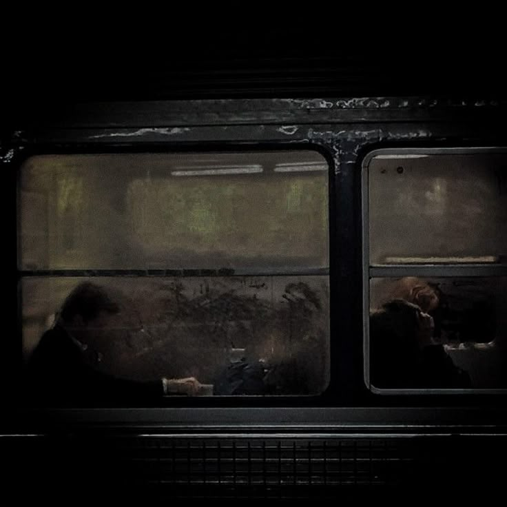 two people sitting on a bus in the dark with their backs to each other, looking out the window