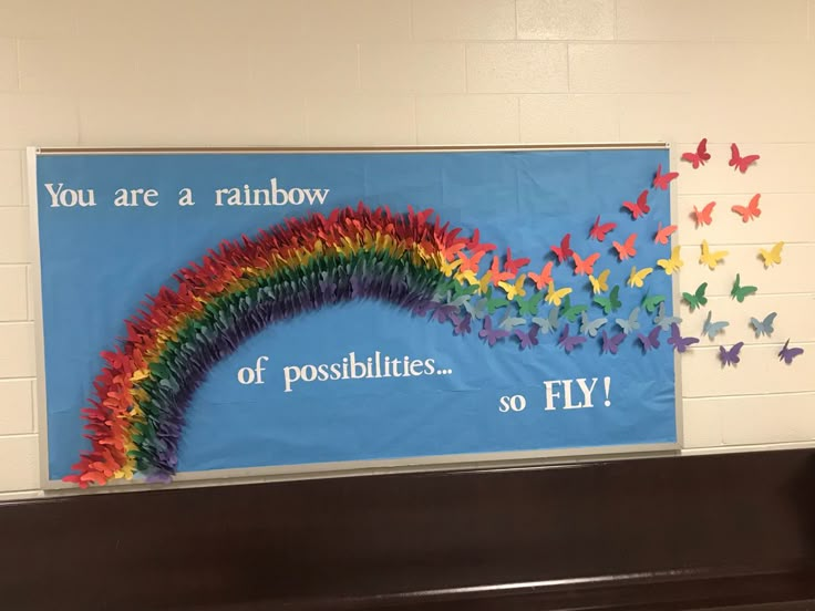 a bulletin board with butterflies on it and a rainbow painted on the wall behind it