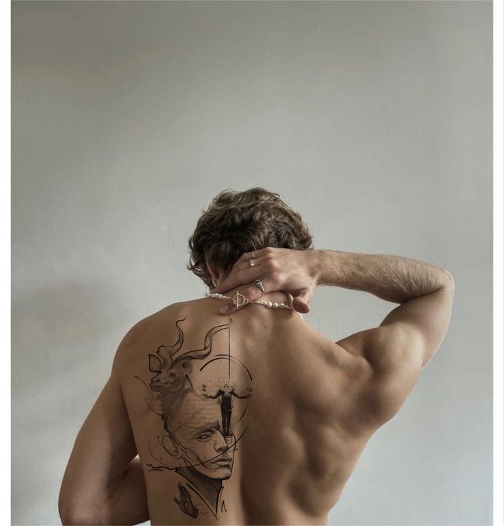 the back of a man with tattoos on his upper and lower half, standing in front of a white wall