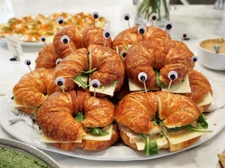 many croissants with googly eyes and cheese on them are arranged on a plate