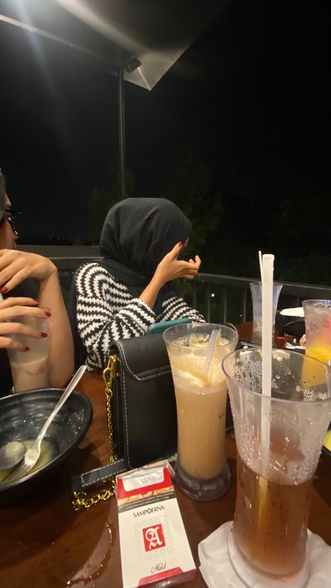 two people sitting at a table with drinks in front of them and food on the side