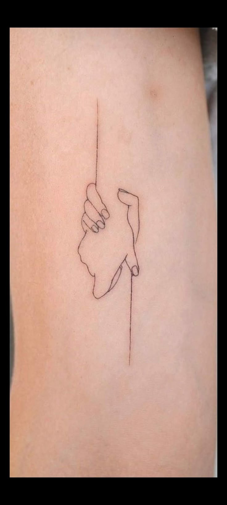 a small tattoo on the back of a woman's thigh, with a line drawing of two hands holding each other