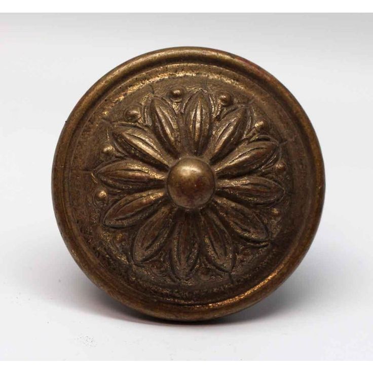 an antique brass door knob with a flower design on the front and center, set against a white background