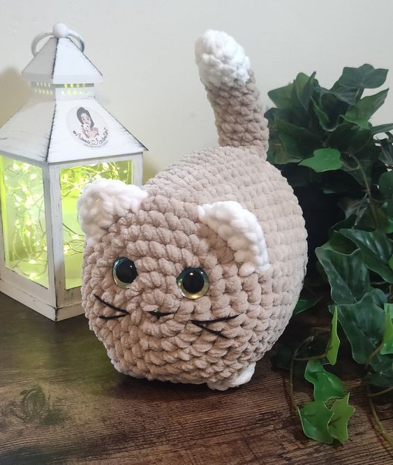 a crocheted cat sitting on top of a wooden table next to a potted plant