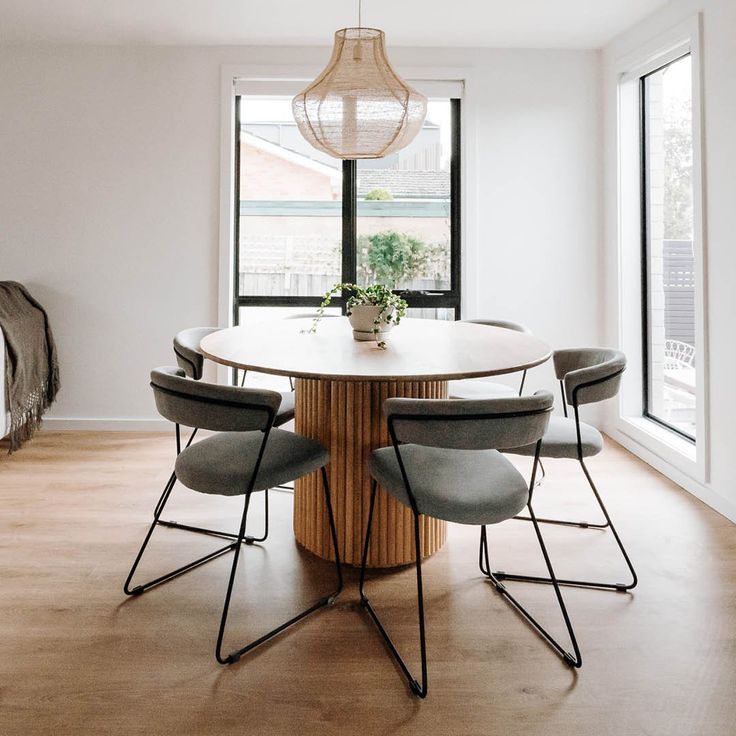 a dining room table with four chairs and a plant in the center surrounded by windows