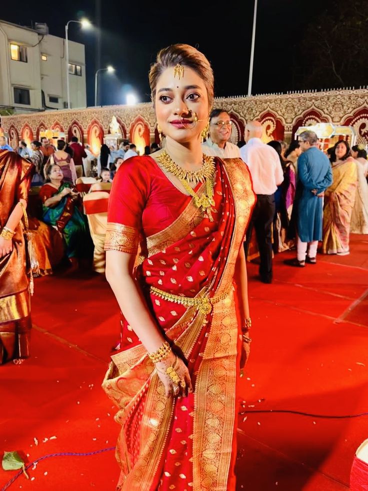 a woman in a red and gold sari standing on a red carpet with other people