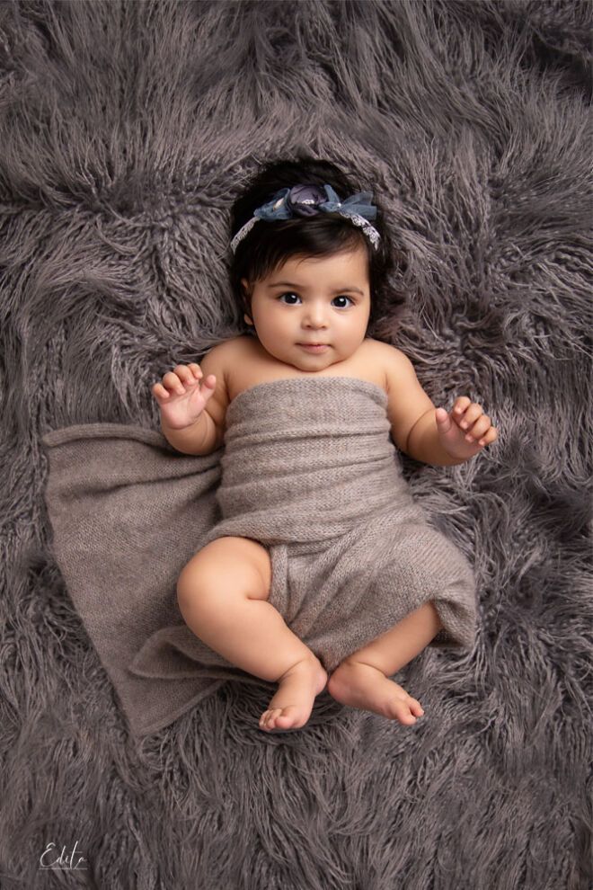 a baby is laying on a fluffy gray blanket and wearing a wrap around her body