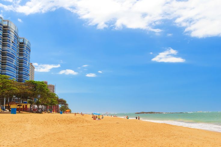 people are walking on the beach in front of some tall buildings and blue skies with white clouds