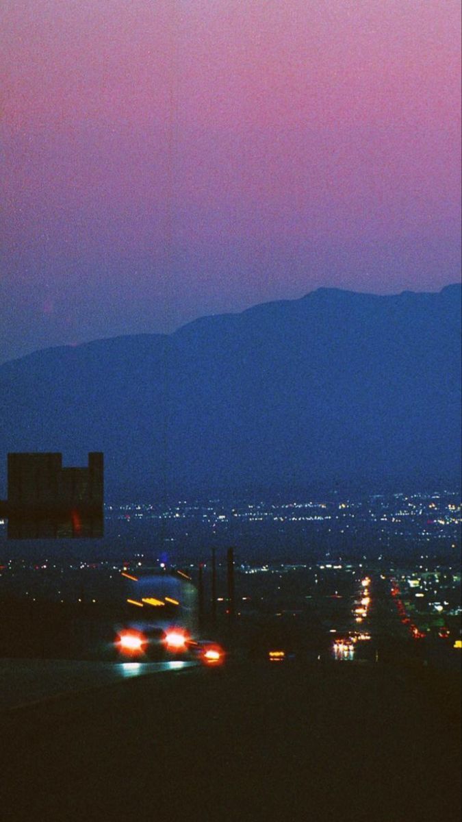 the city lights shine brightly at night as seen from an overpass with mountains in the background