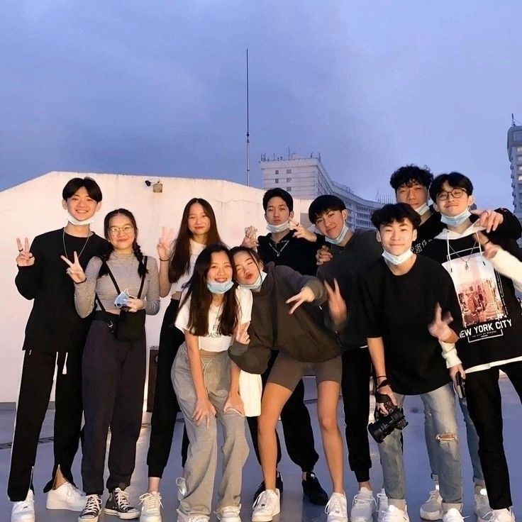 a group of young people standing next to each other in front of a building with their hands up