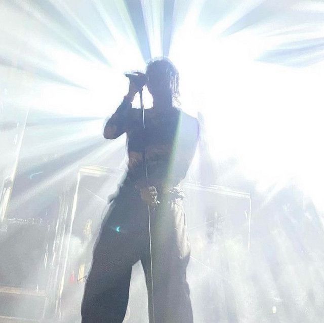 a man standing on top of a stage holding a microphone in his hand and wearing all black