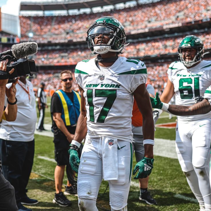 a football player is standing on the field with his helmet in hand and other players behind him