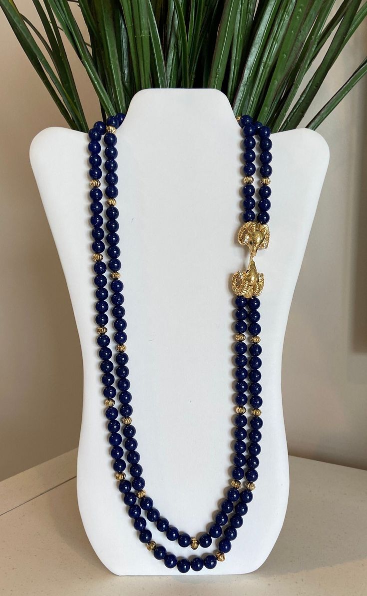 Kenneth Jay Lane's royal blue faux lapis beaded double strand necklace with double gold plated ram's heads encrusted with clear rhinestones and green rhinestone eyes. This was by designer Kenneth Jay Lane for Avon and in excellent condition. Please see pictures and video for description. Signed K.J.L. for Avon at clasp. Please visit my shop for more vintage jewelry: https://vintagetimejewelry.etsy.com/ Blue Beads Necklace, Ram Head, Rhinestone Eyes, Blue Beaded Necklace, Double Strand Necklace, Kenneth Jay Lane, Strand Necklace, Blue Beads, Clear Rhinestones