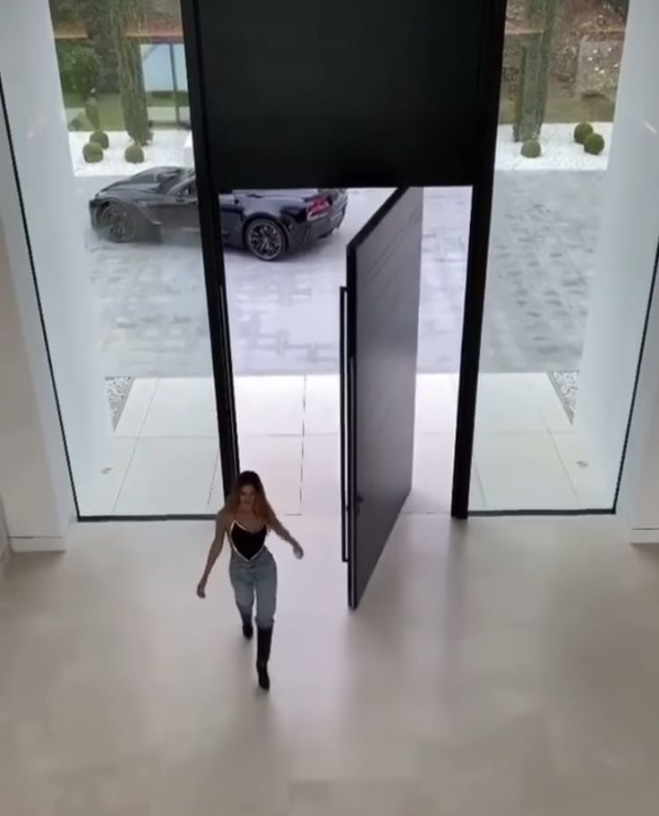 a woman is walking out of an open door into a car parking lot in front of her